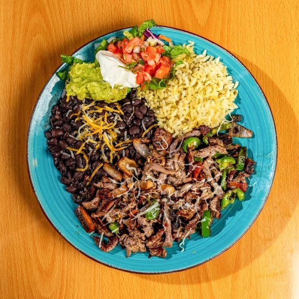 A vibrant Mexican dish with steak, rice, black beans, guacamole, pico de gallo, and salad.