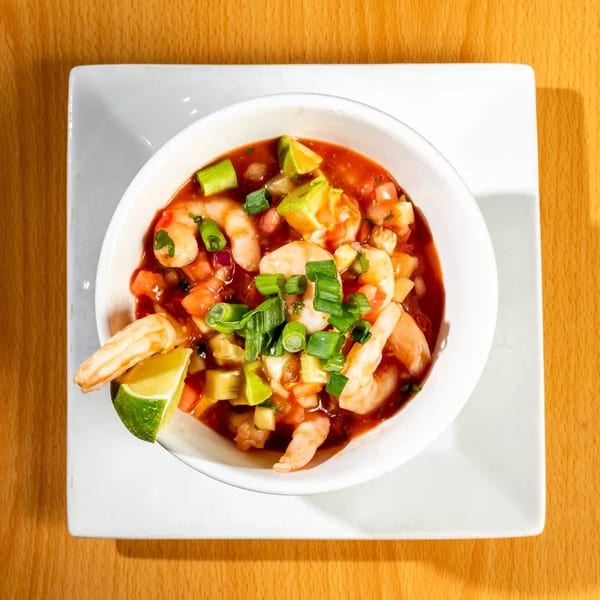 Shrimp ceviche with avocado, tomatoes, and green onions in a white bowl on a wooden table.