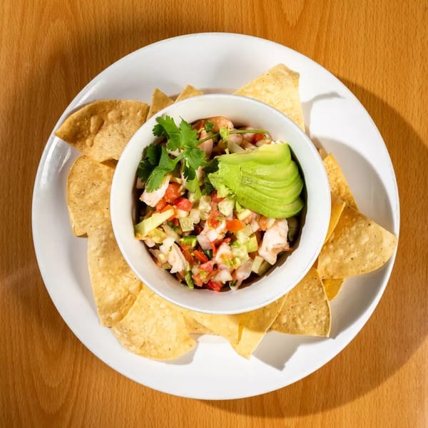 A bowl of fresh shrimp ceviche with avocado and cilantro, surrounded by tortilla chips.