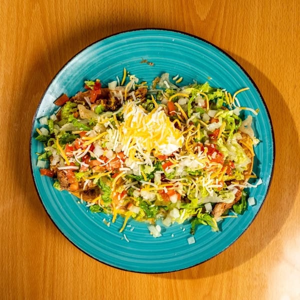 Overhead view of a taco salad with lettuce, tomatoes, cheese, and sour cream on a blue plate.
